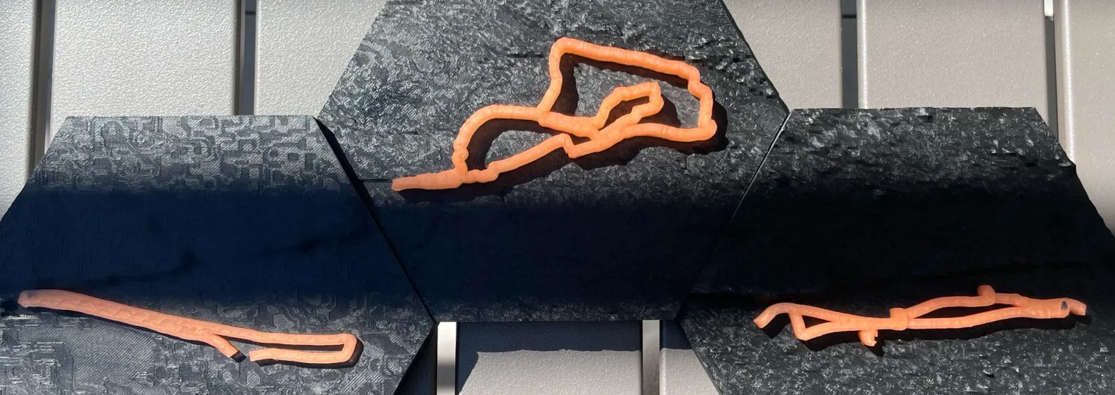 Three 3D printed terrain trophy hexagons with orange swim, bike and run routes from one Ironman triathlon