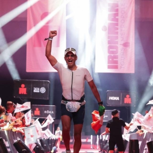 My dad crossing the Ironman finish line at night, one arm raised, under the finish arch