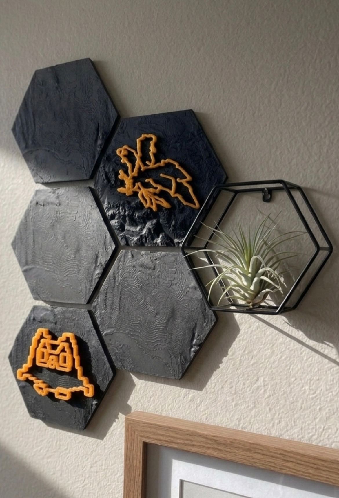 Six 3D printed terrain trophy hexagons tiled on a wall, two showing UV-reactive orange race routes